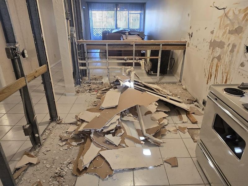 Kitchen mid-demolition with drywall removed and debris on the floor, ready for haul-off