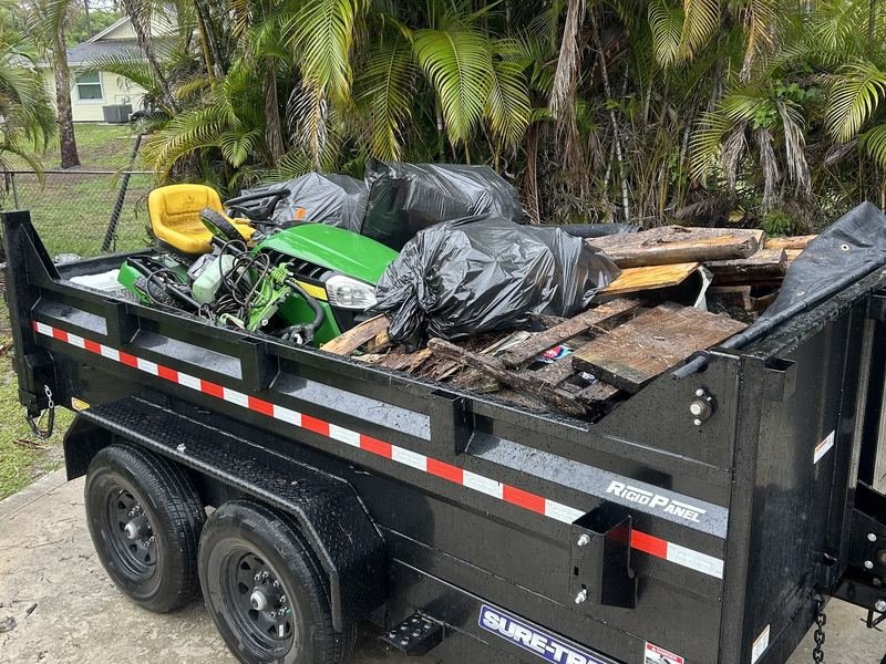 Dump trailer loaded with a ride-on mower, bagged waste and scrap timber